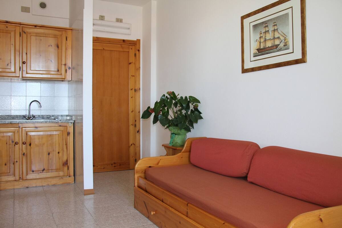 A kitchen with wooden cabinets and a sink, a wooden door, a red sofa, and a framed picture on the wall.