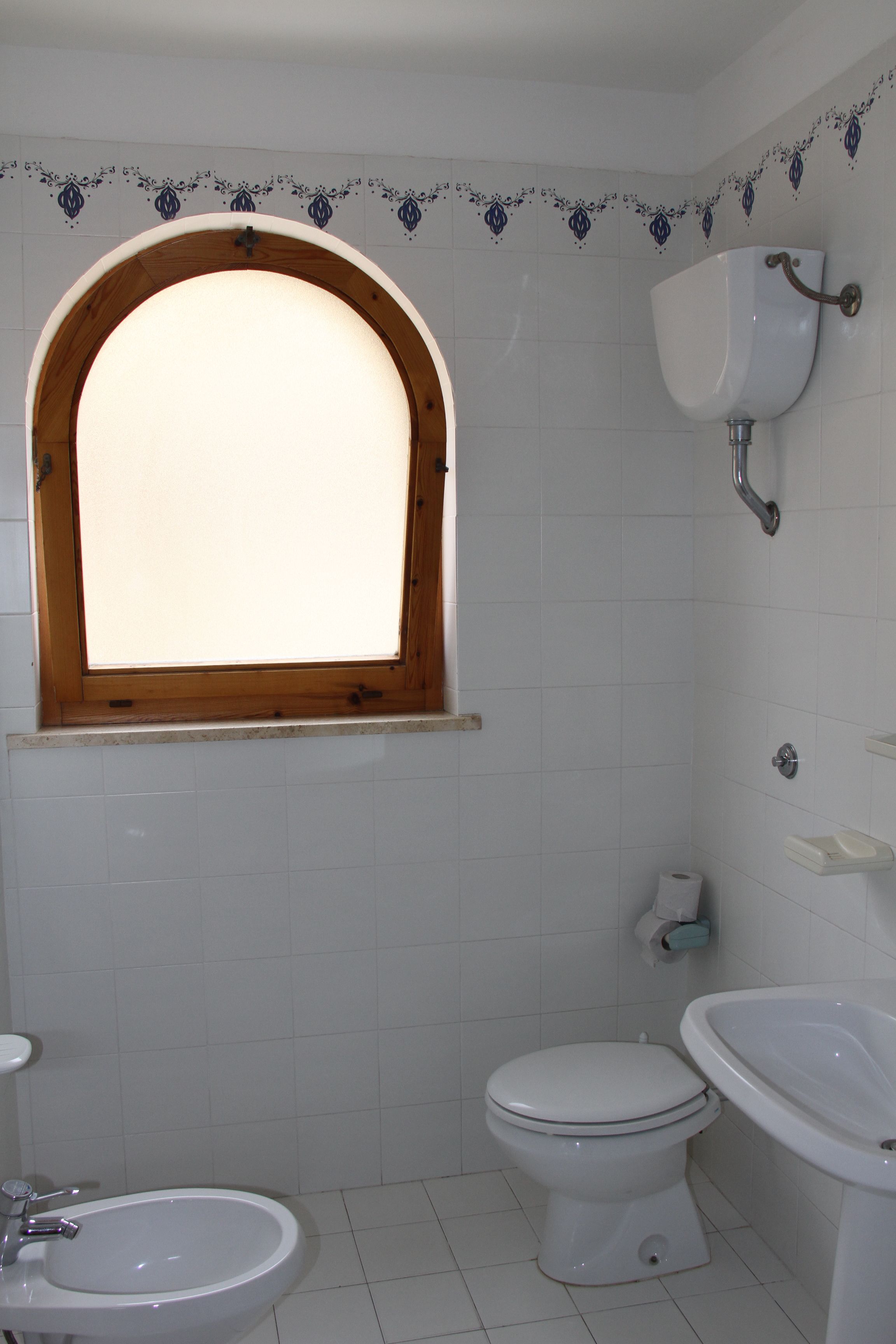 A bathroom with a window, a toilet, a bidet, and a sink.