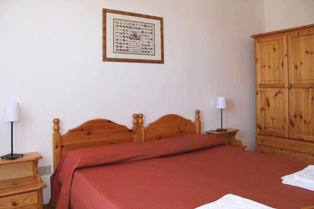 A neatly made bed with a wooden headboard, two bedside tables with lamps, and a wooden wardrobe.
