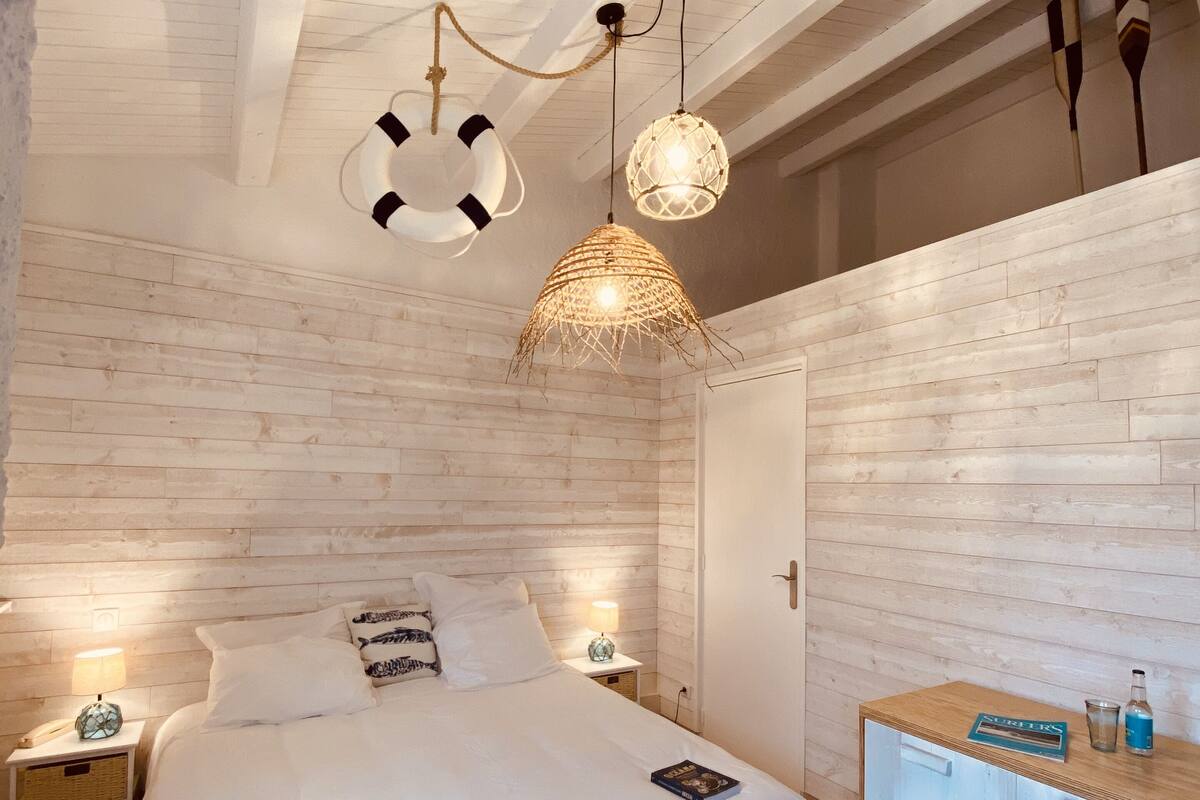 Une chambre à coucher comprenant un lit, des tables de chevet, une commode et un luminaire suspendu.