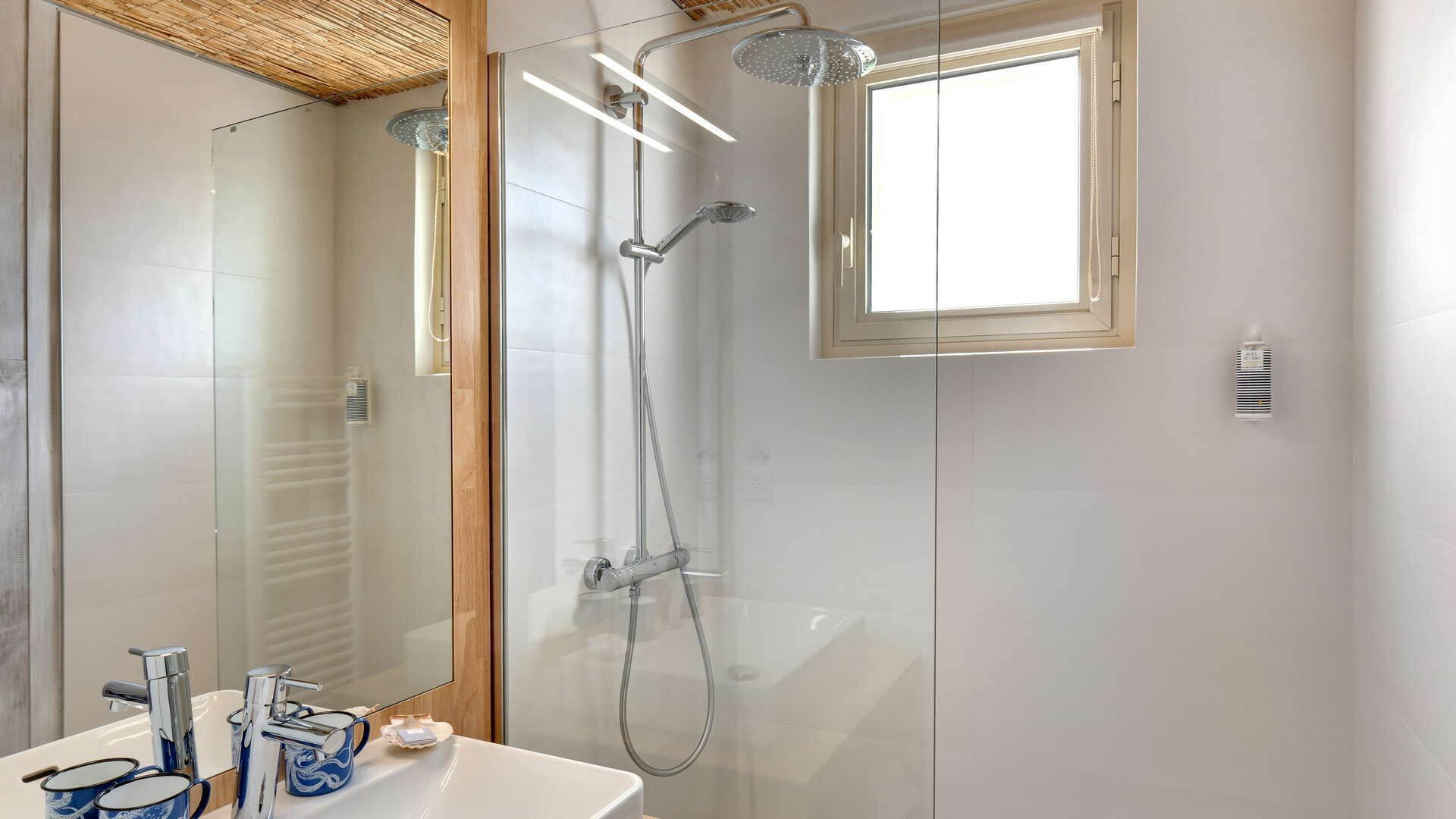 A modern bathroom with a glass-enclosed shower, a large mirror, and a white sink with two faucets.