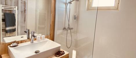 A modern bathroom with a large mirror, a wooden vanity, a glass-enclosed shower, and a small window.