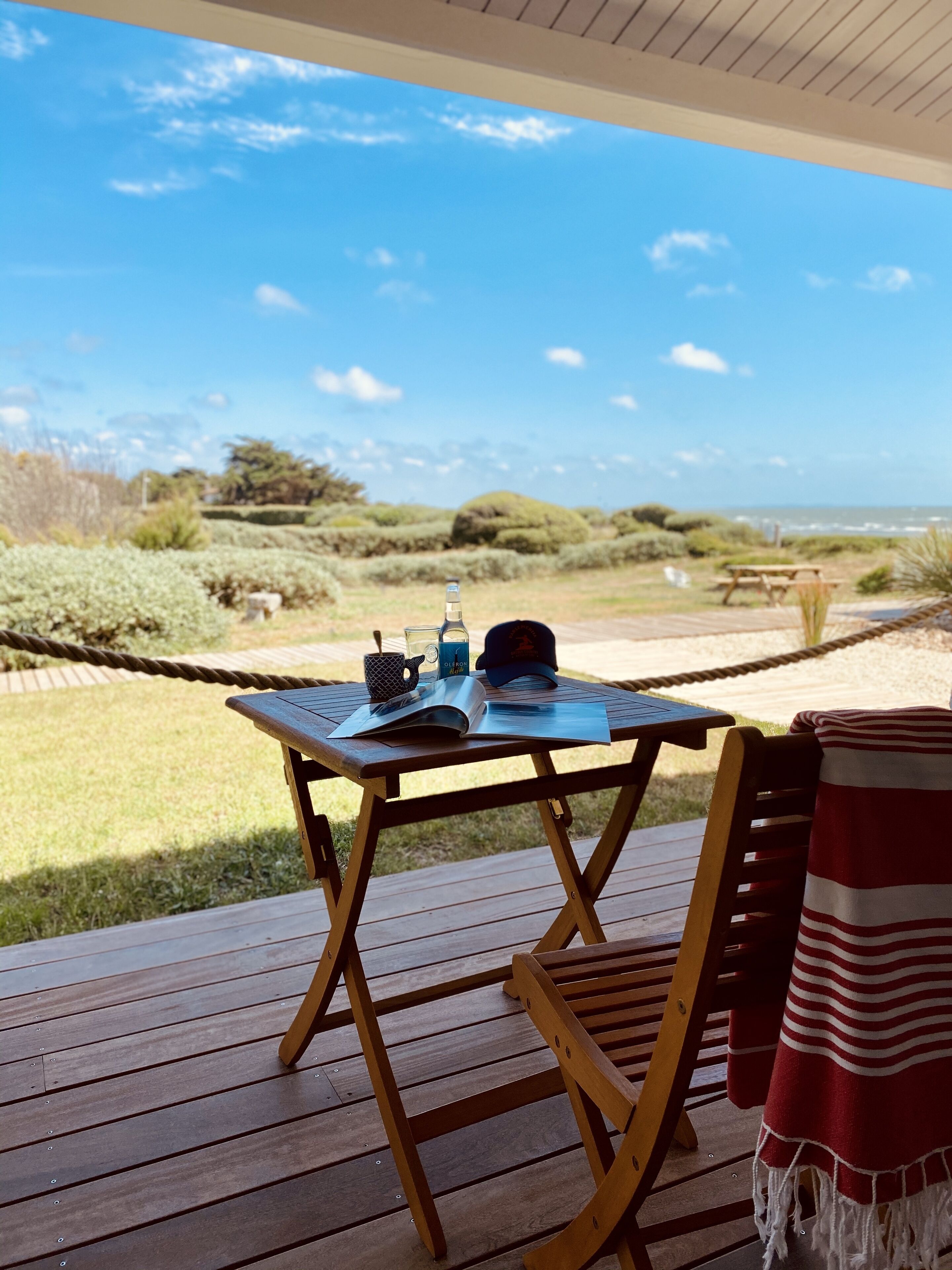 A wooden deck with a table and chairs, overlooking a beach with a clear sky.