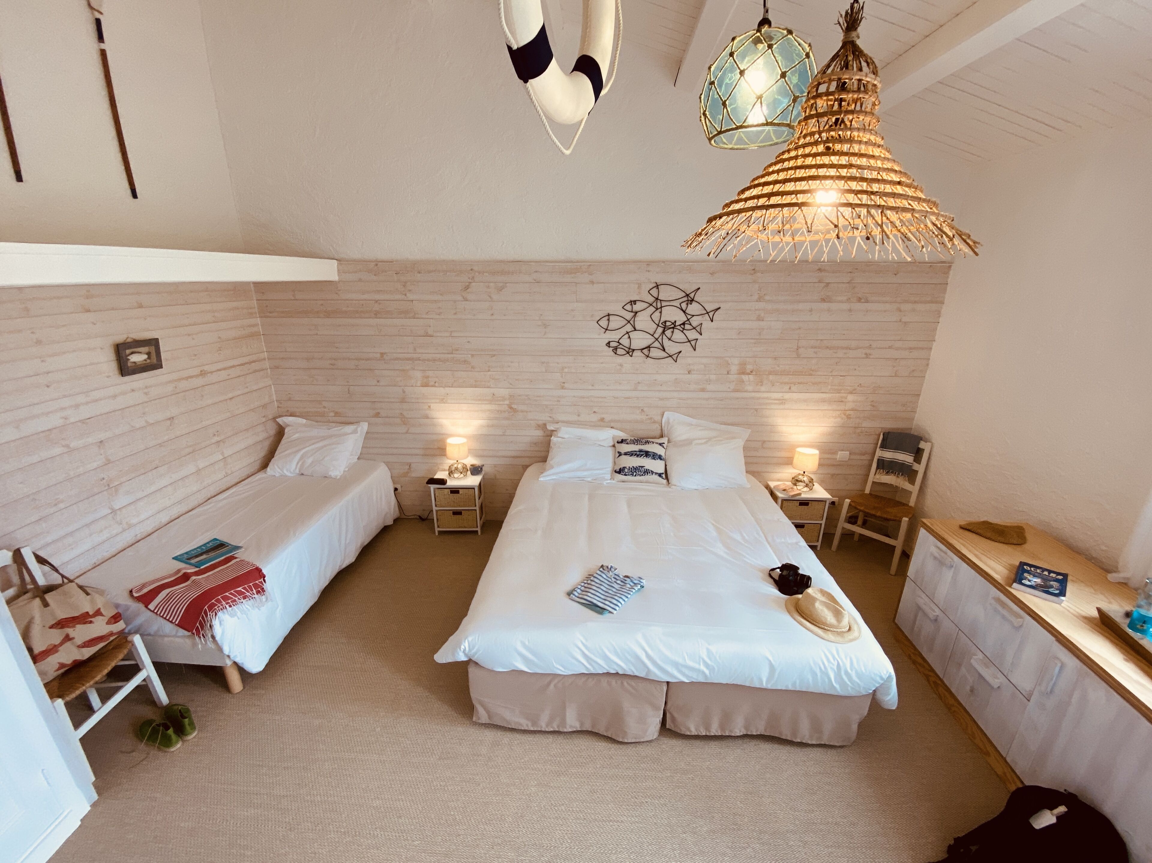 Una habitación con dos camas individuales, una cama más grande, un escritorio y una lámpara colgante.