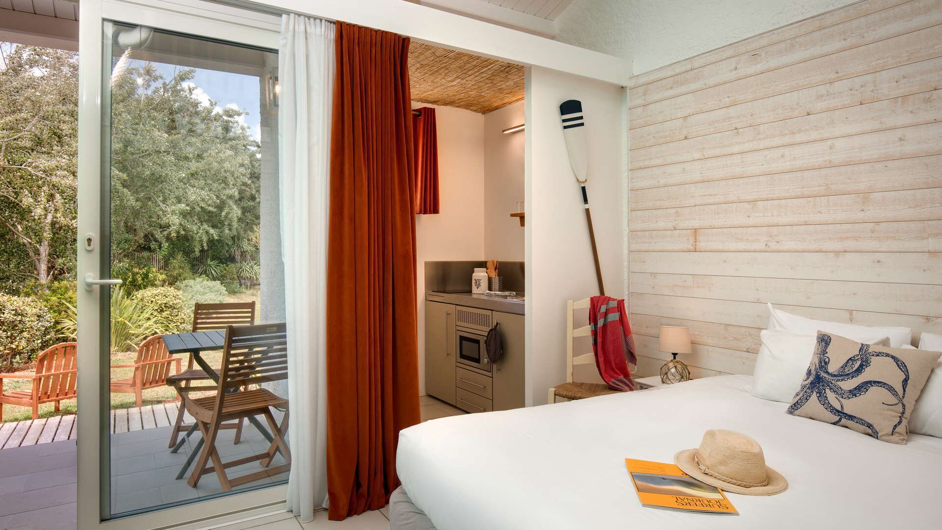 A bedroom with a bed, a dining table, and chairs outside a sliding glass door.
