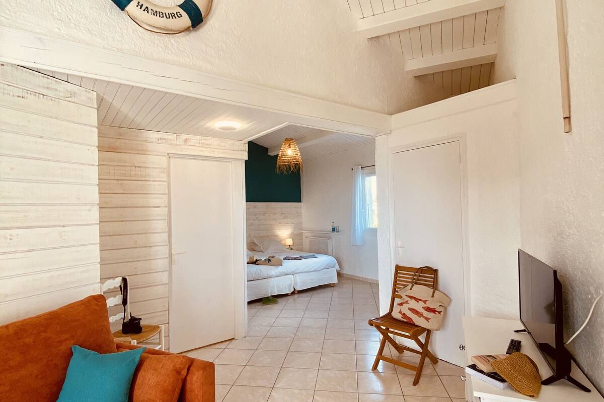 Une pièce spacieuse avec un grand canapé orange, une chaise en bois, un téléviseur et un lit à l’arrière-plan.
