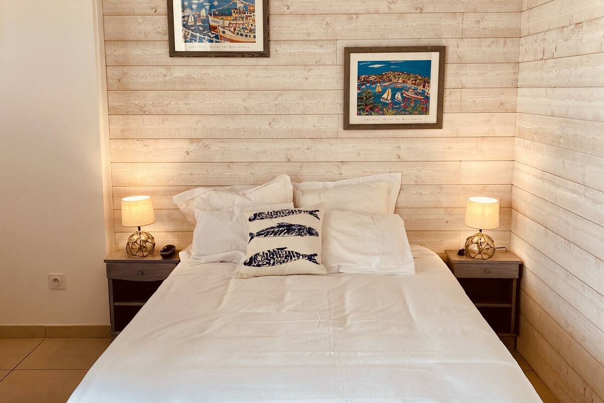 Une chambre avec un mur en bois, un lit recouvert de linge de lit blanc, deux tables de chevet avec des lampes et deux tableaux encadrés accrochés au mur.
