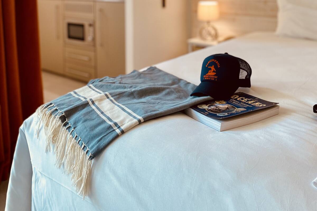 Une chambre d’hôtel avec un lit, un livre, une casquette et une table de chevet.