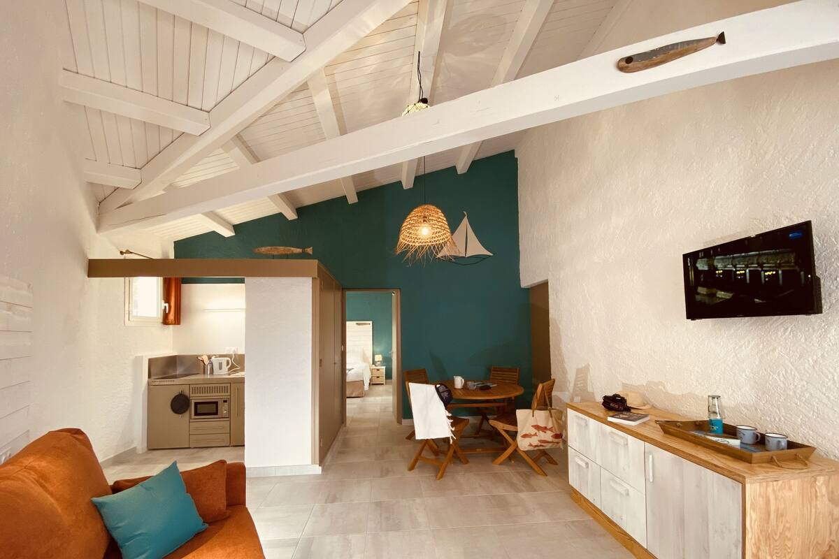 Une cuisine moderne avec un plan de travail en bois, un coin repas avec une table et des chaises, et un salon avec un canapé et un téléviseur.