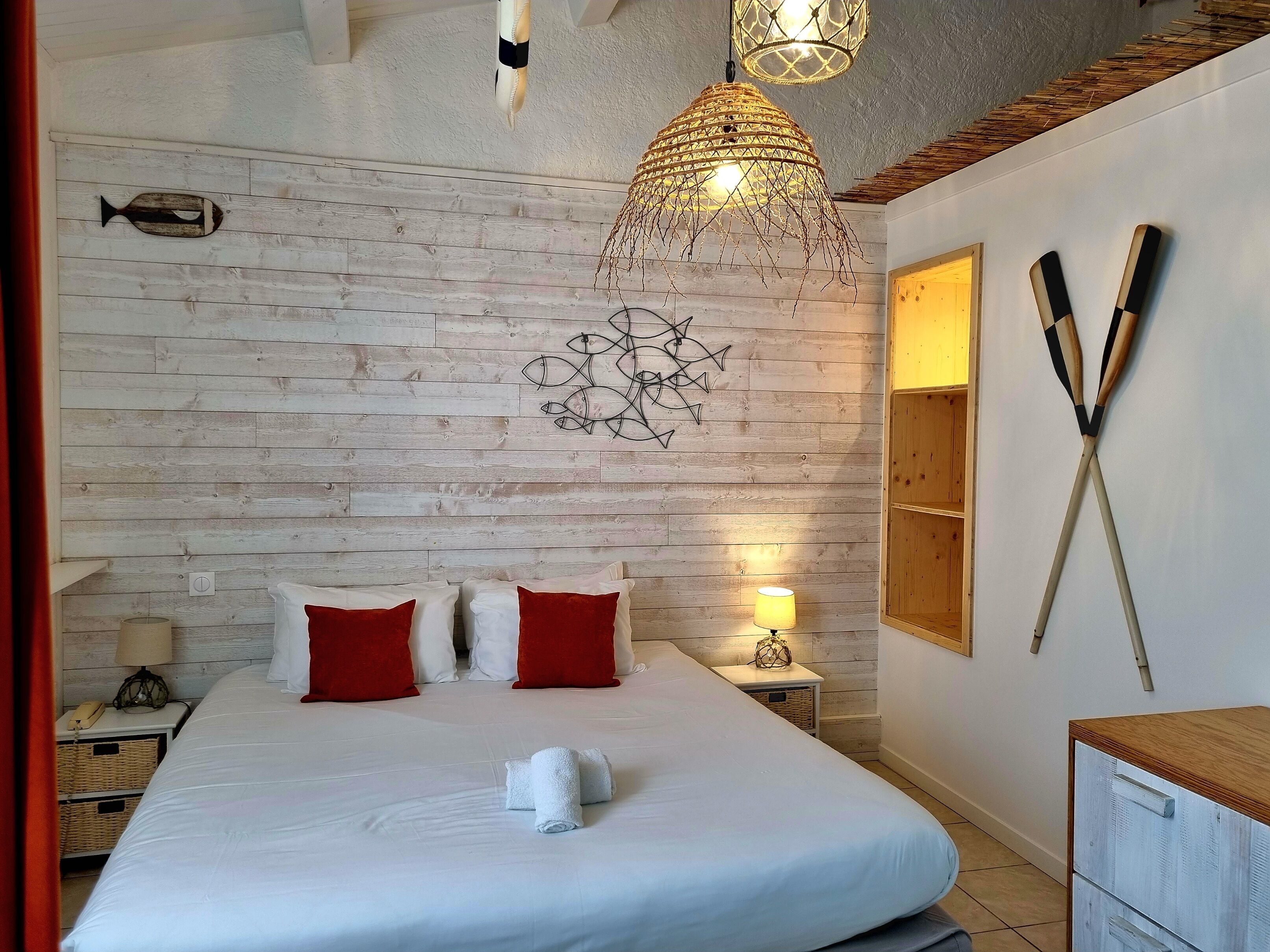 A hotel room with a wooden wall, a bed with white and red pillows, a bedside lamp, and a fish decoration.