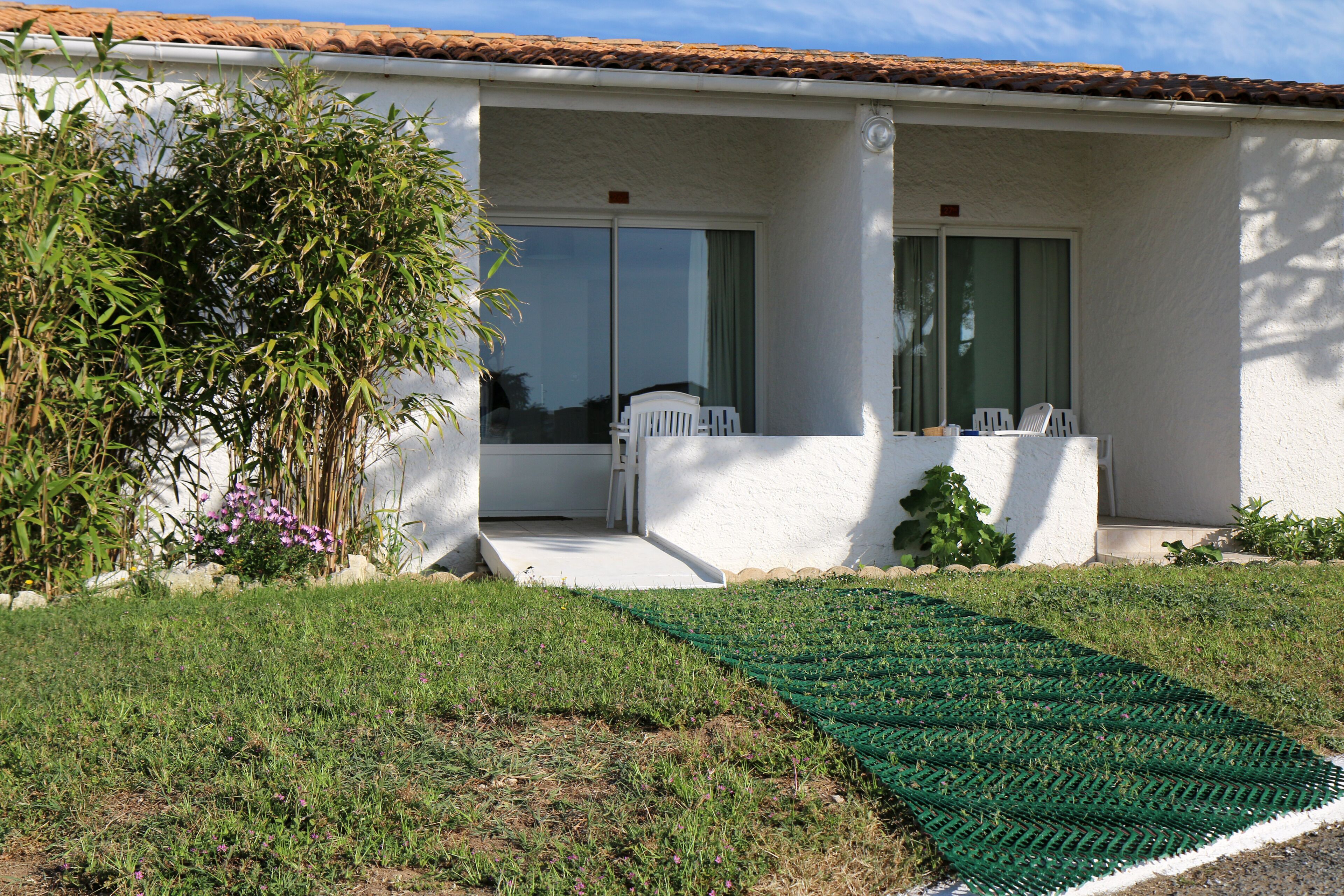 A house with a covered porch, a small garden with a green mat, and a white fence.