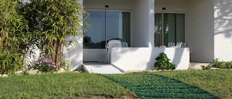 A house with a covered porch, a small garden with a green mat, and a white fence.