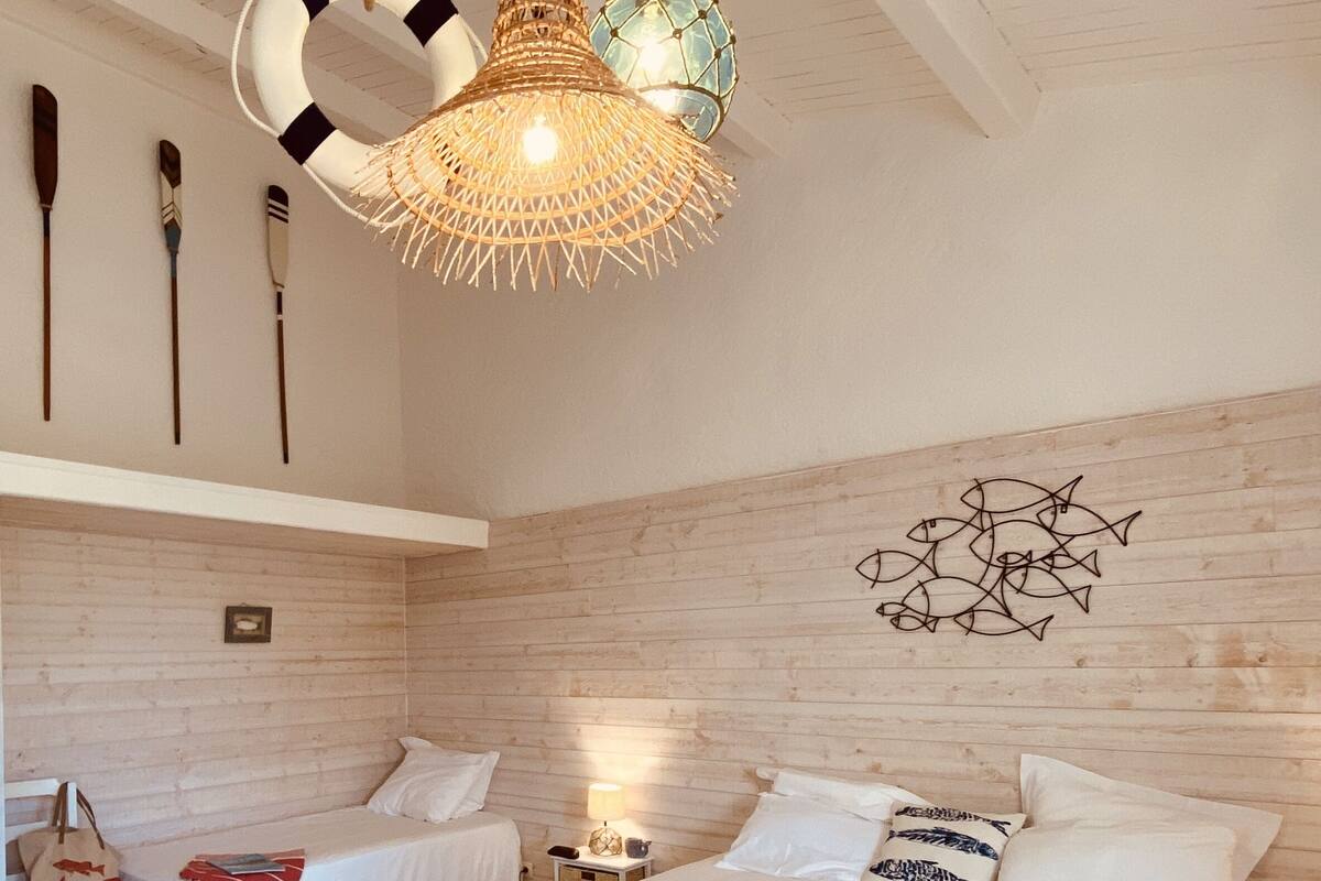 Une chambre avec deux lits, un mur en bois, une fresque murale représentant des poissons et un luminaire original en fibres tressées.