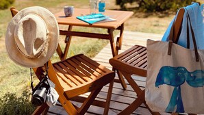 Een houten terras met een tafel, stoelen, een hoed, een camera en een tas.