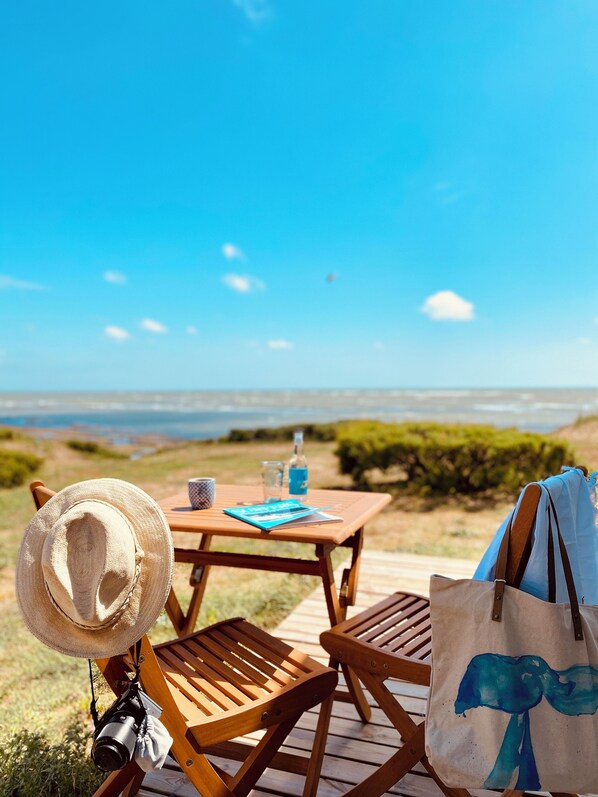 A wooden deck with a table and chairs, a hat, a camera, and a tote bag.