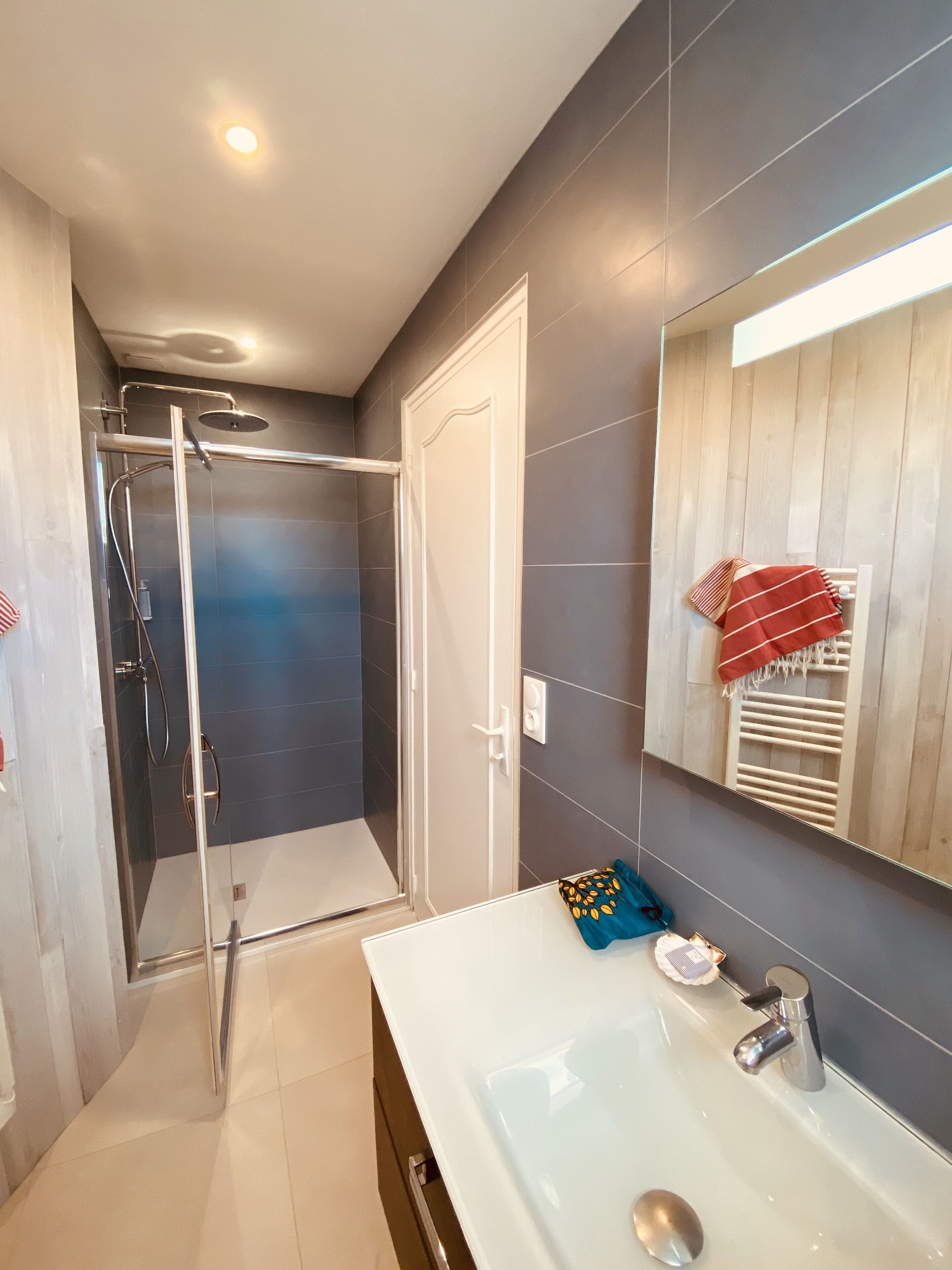 A modern bathroom with a glass shower enclosure, a white sink with a mirror, and a towel rack with a red towel.