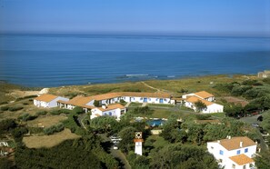 A coastal motel with multiple white buildings, a sign indicating a motel, and a view of the ocean.