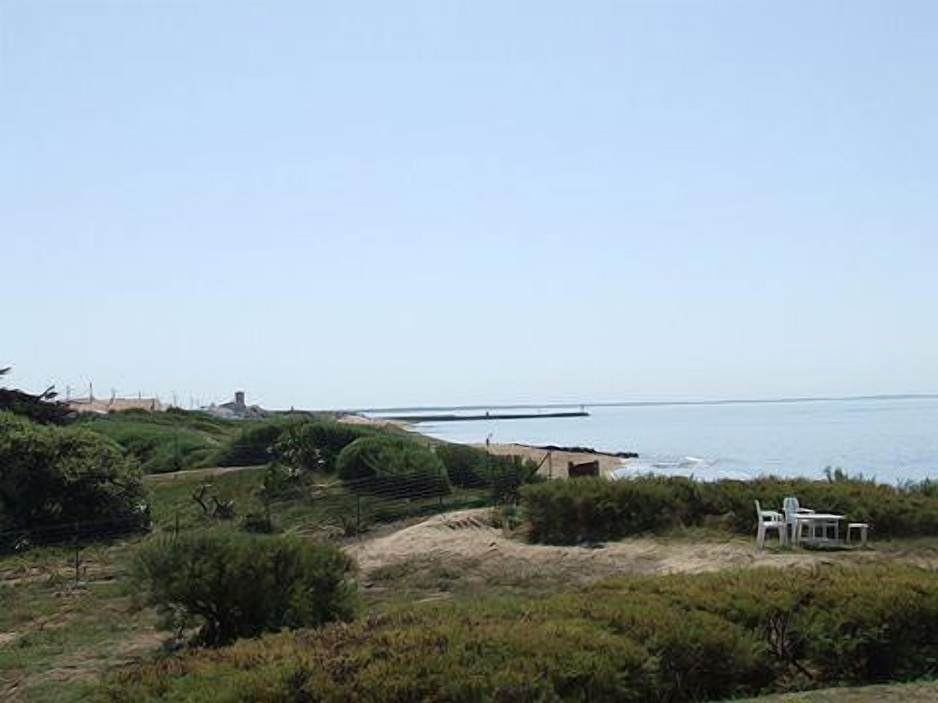 A coastal landscape with a beach, a small structure, and a table with chairs.