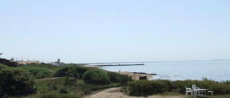 A coastal landscape with a beach, a small structure, and a table with chairs.