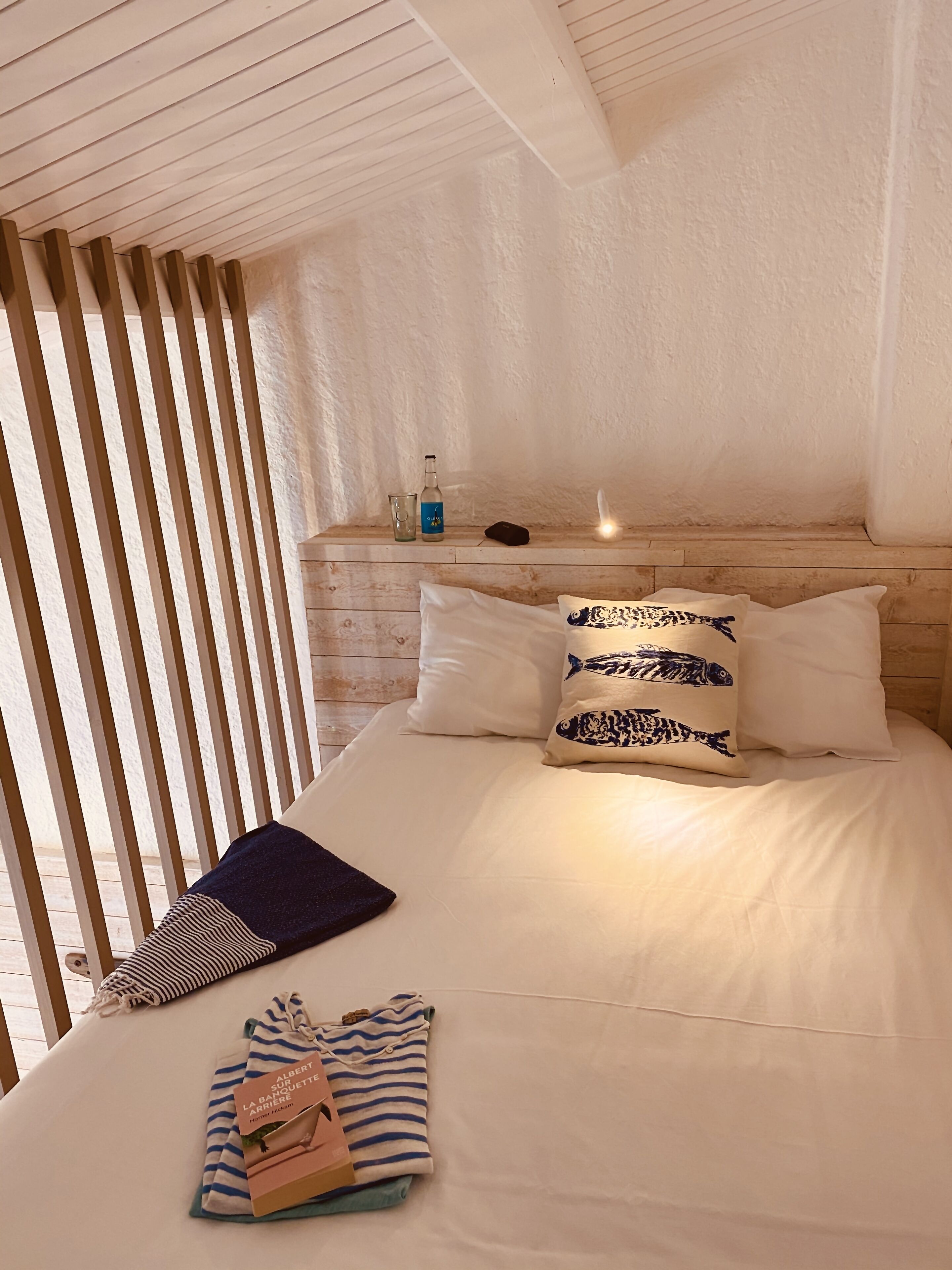 A neatly made bed with pillows, a bedside table with a bottle and glass, and a striped towel on the bed.