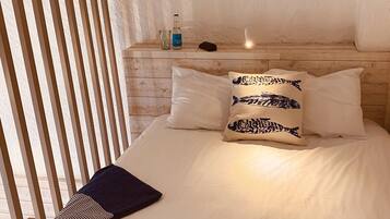 A neatly made bed with pillows, a bedside table with a bottle and glass, and a striped towel on the bed.