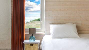 A bedroom with a wooden wall, a bed, a nightstand with a lamp, and a window with curtains.