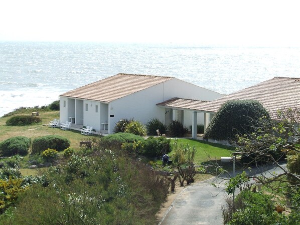 A coastal building with a tiled roof, a covered patio, and a view of the sea.