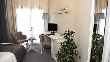 Habitación de hotel con una cama, un escritorio, una silla, un televisor, una mesita con un libro y un jarrón, y una planta en maceta.