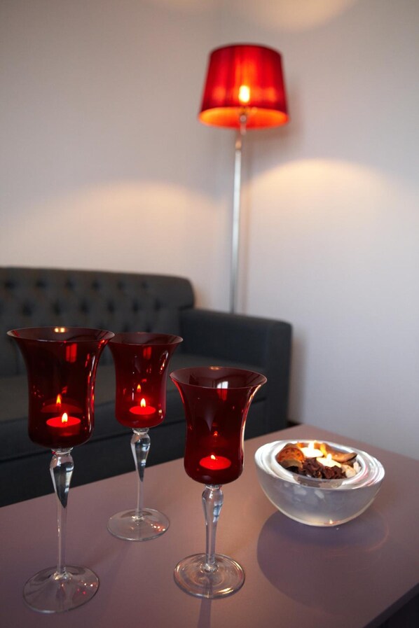Three red candle holders on a table, a bowl with a candle, and a red lamp in the background.