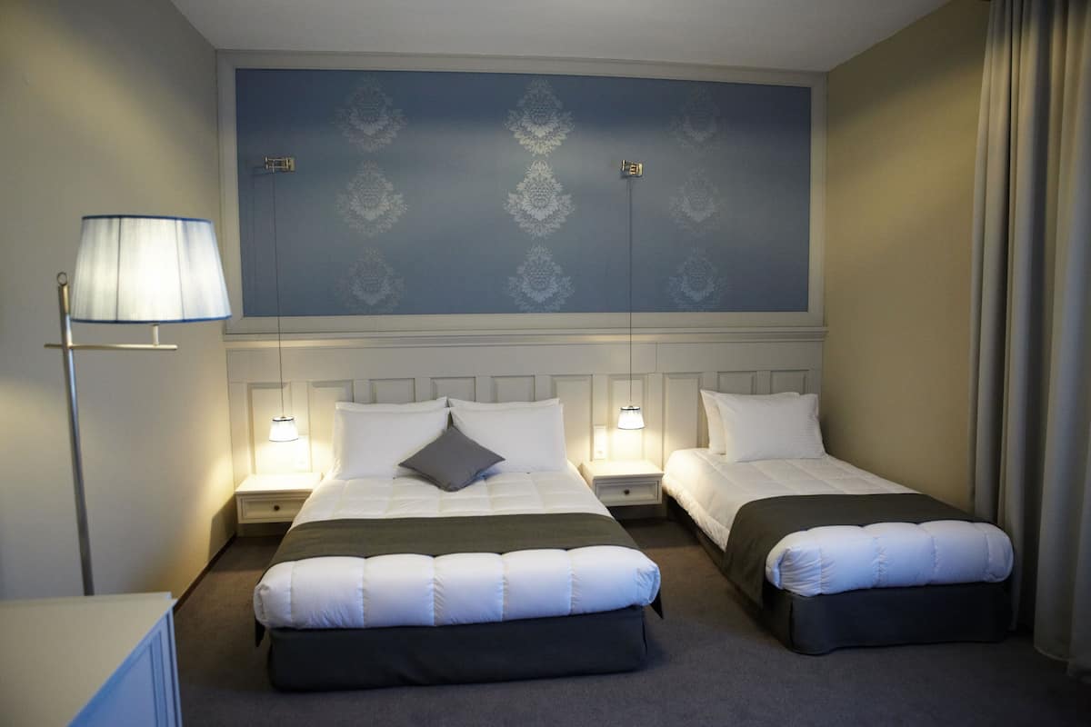 A hotel room with two beds, a nightstand with a lamp, and a wall with a decorative pattern.