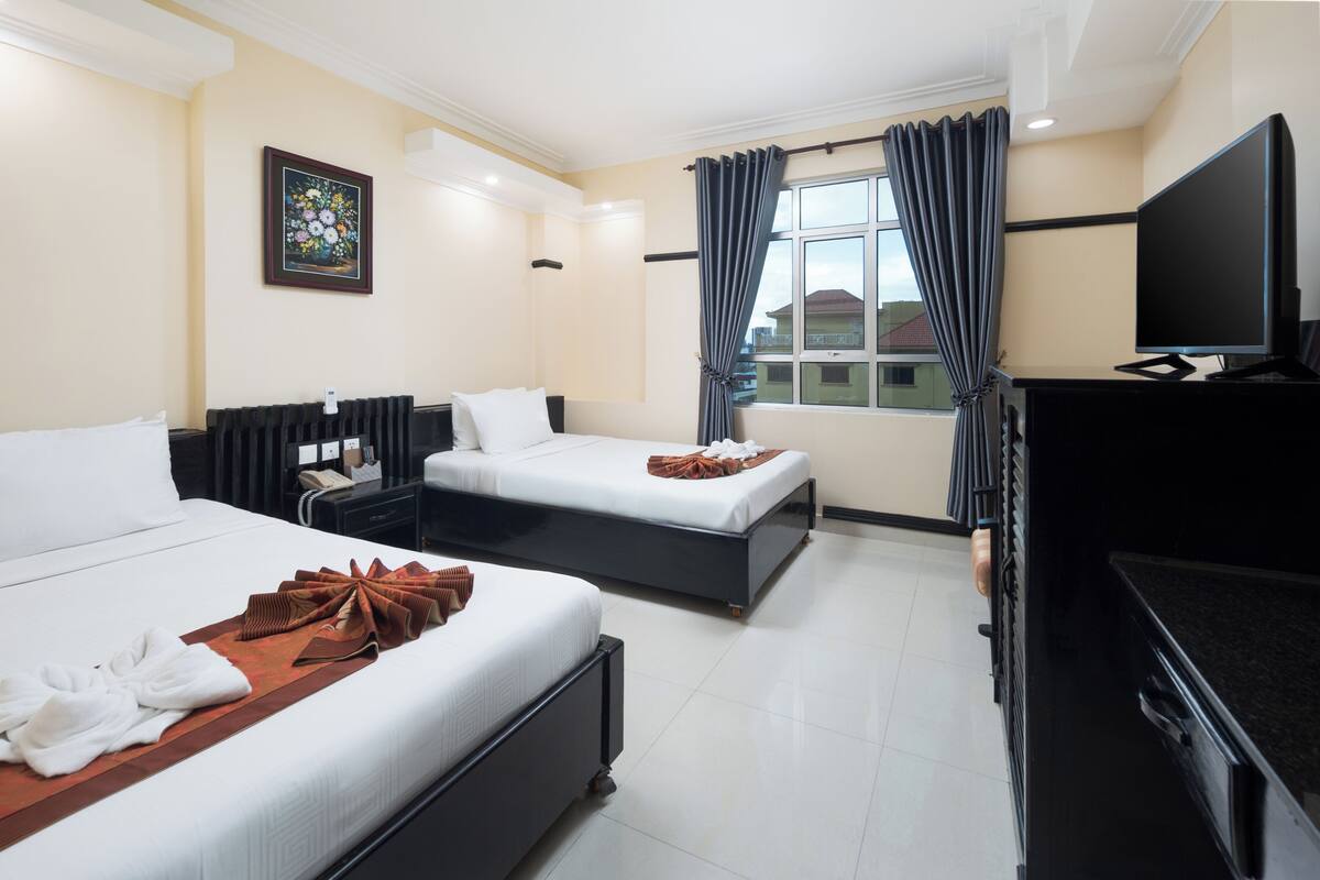 A hotel room with two beds, a flat-screen TV, a desk, and a window with curtains.
