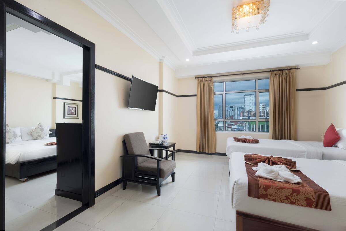 A hotel room with two beds, a TV, a chair, a small table, and a window with a city view.