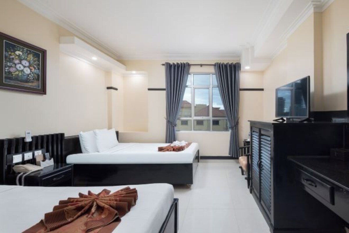 A hotel room with two beds, a TV, a desk, and a window with curtains.