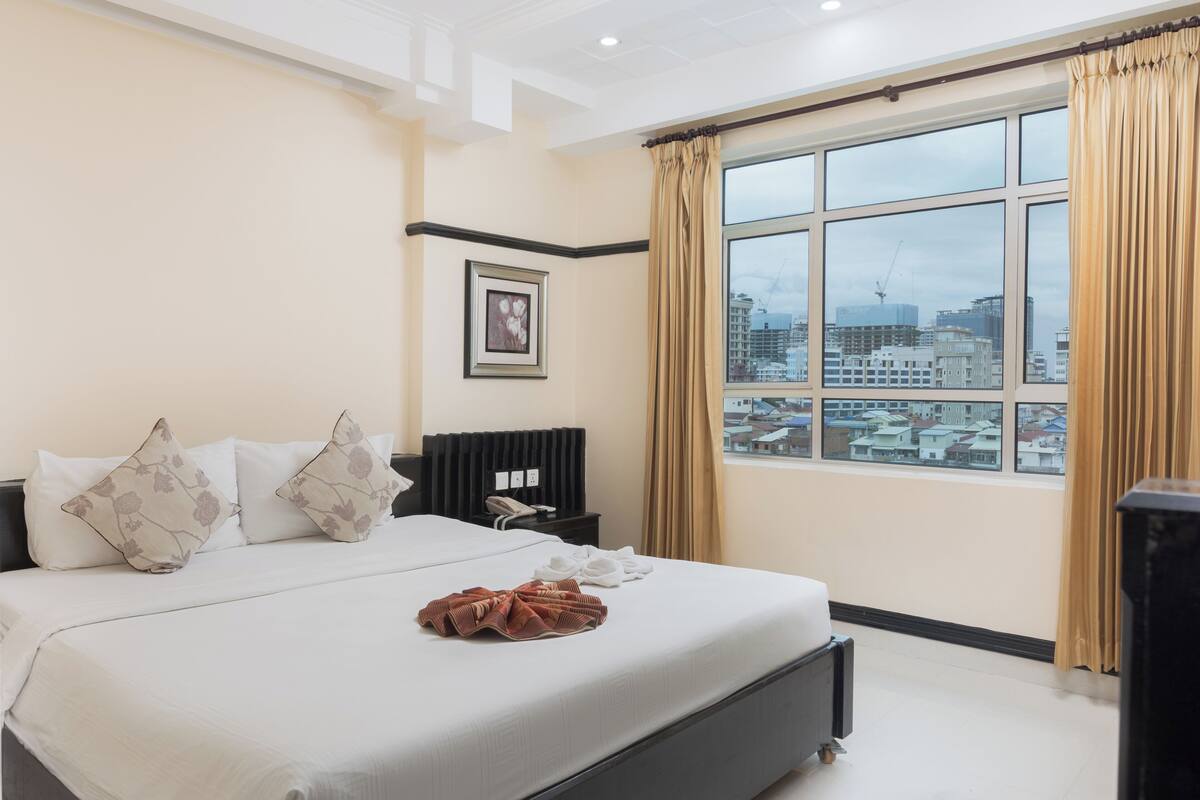 A hotel room with a large bed, a nightstand, a framed picture on the wall, and a window with curtains.