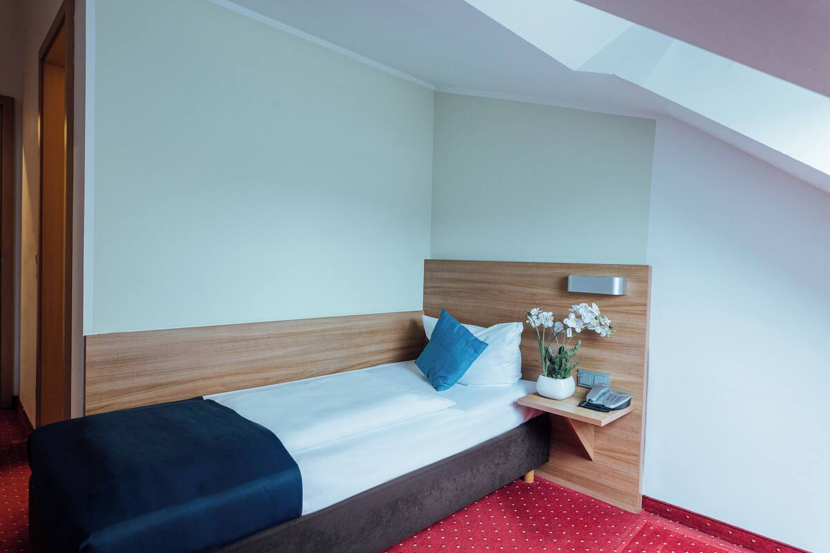 Hotellihuone, jossa on sänky, yöpöytä, jossa on puhelin, ja pieni ruukkukasvi.
