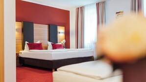 A hotel room with a large bed, a bedside table, a nightstand, and a window with curtains. - Hotel Andra (Munich)