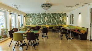 A restaurant with multiple tables and chairs, a patterned wall, and a chandelier. - Hotel Andra (Munich)