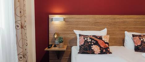 A hotel room with a wooden headboard, a bedside table with a lamp, a phone, and a decorative plant.