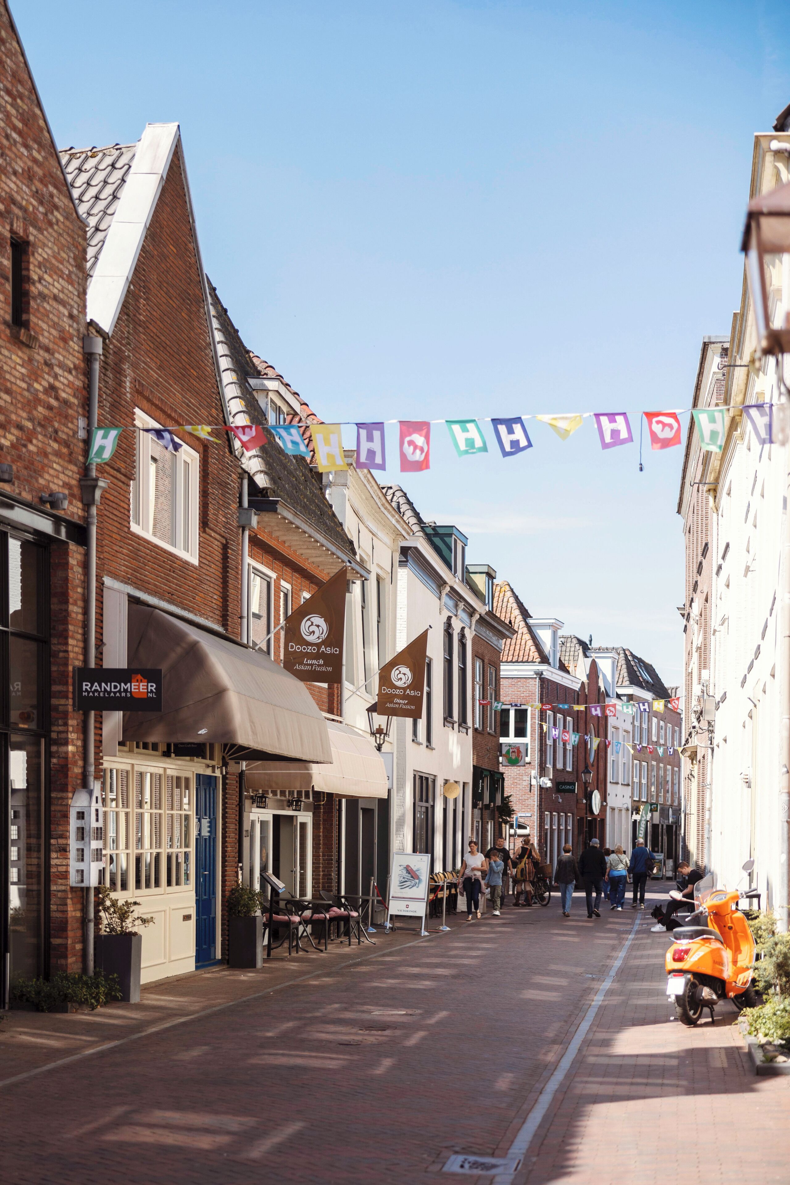 A narrow street lined with traditional buildings, some with awnings and signage, under clear skies.