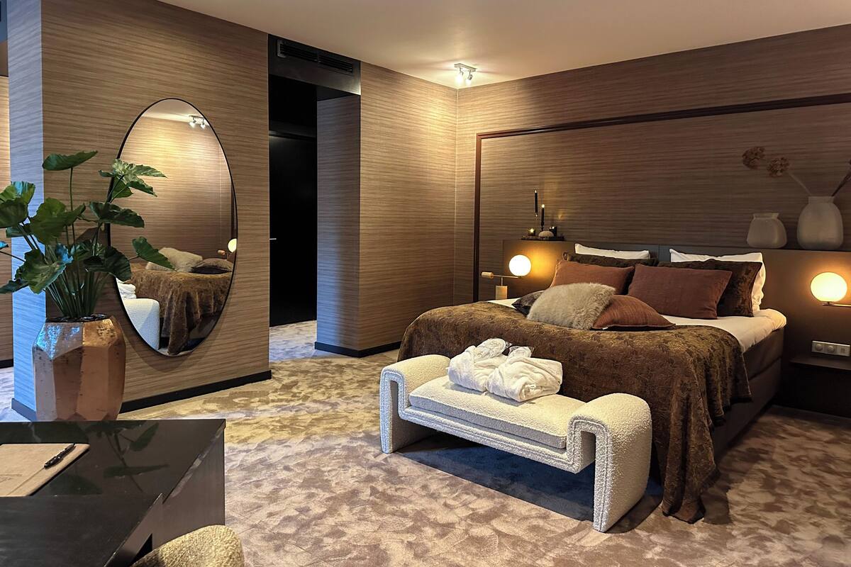 Ein modernes Schlafzimmer mit einem großen Bett, Nachttischlampen, einem Spiegel und einer Topfpflanze.