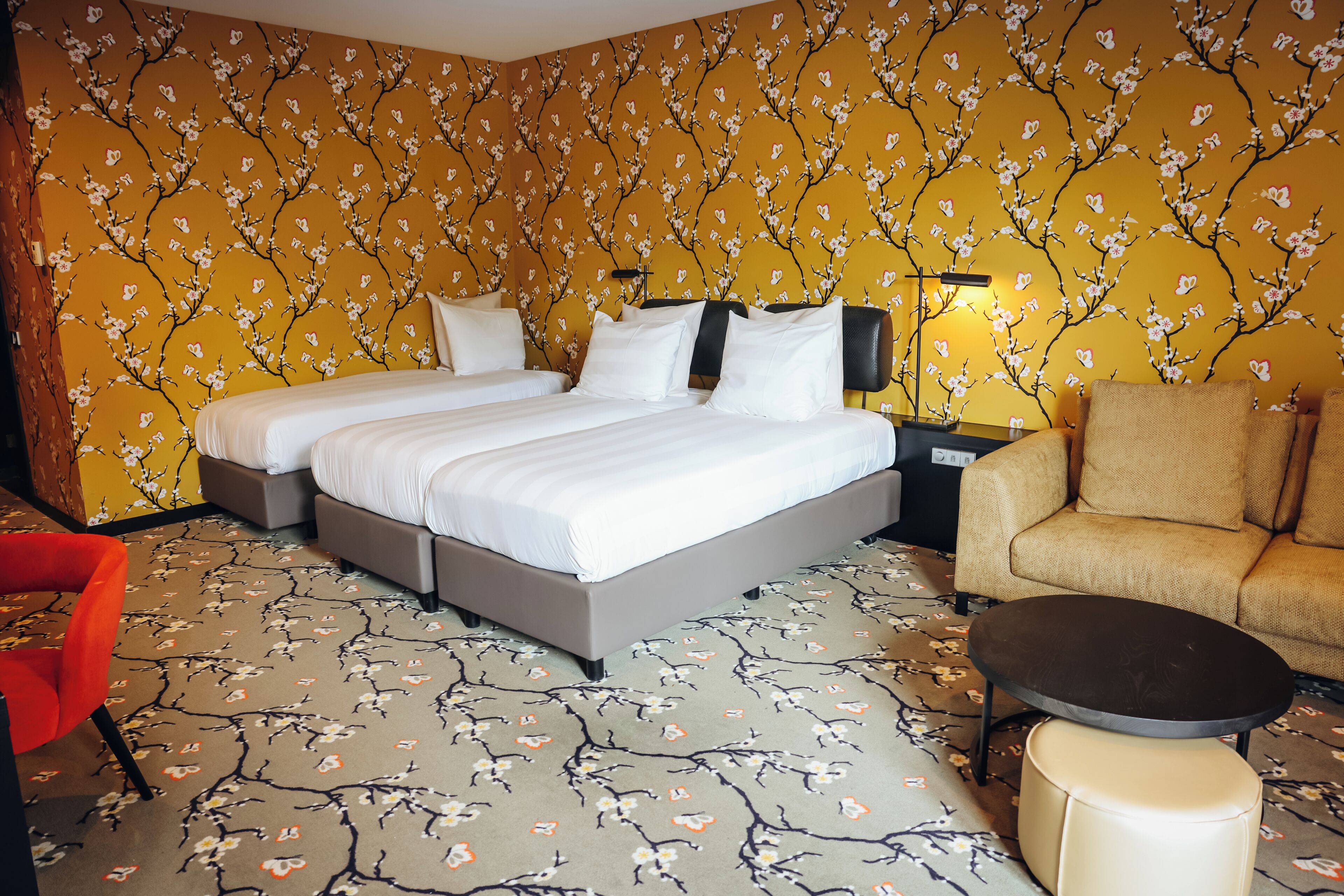 A hotel room with a double bed, a sofa, a small table, and a red chair.