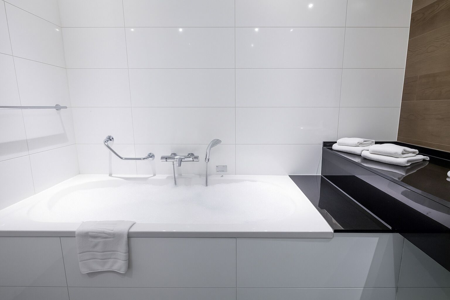 Un baño moderno con una bañera blanca grande, una zona de ducha independiente y un mostrador negro con toallas.