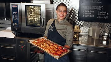 Een keuken met roestvrijstalen apparatuur, een krijtbordmenu en een persoon die een schaal gebak vasthoudt.