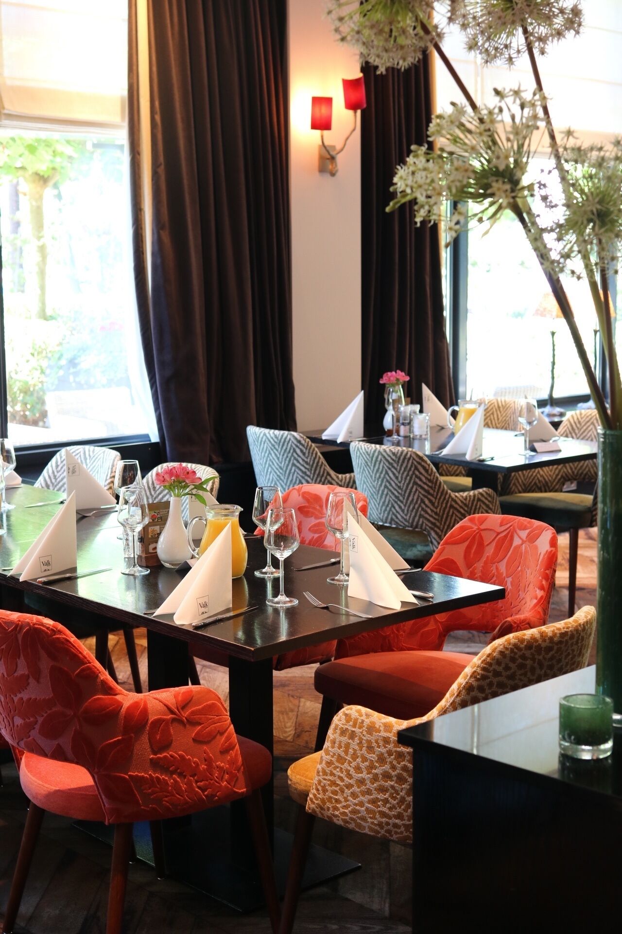 A dining area with tables set for two, each with a menu, wine glass, and a vase with flowers.