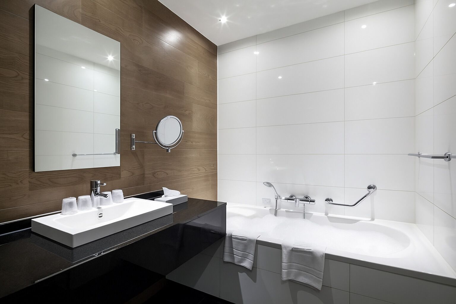 Un baño moderno con tocador doble, un espejo grande, un espejo redondo y una ducha a ras de suelo con puerta de cristal.