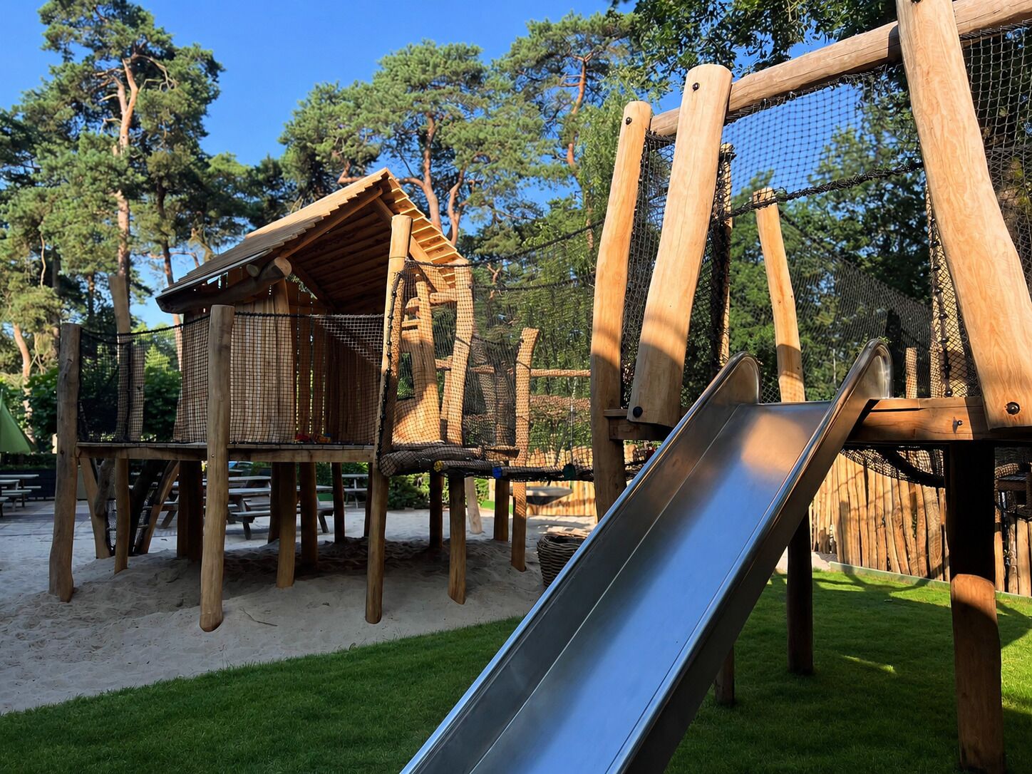 Een speeltuin met een houten glijbaan, klimconstructies en een klein houten huisje.