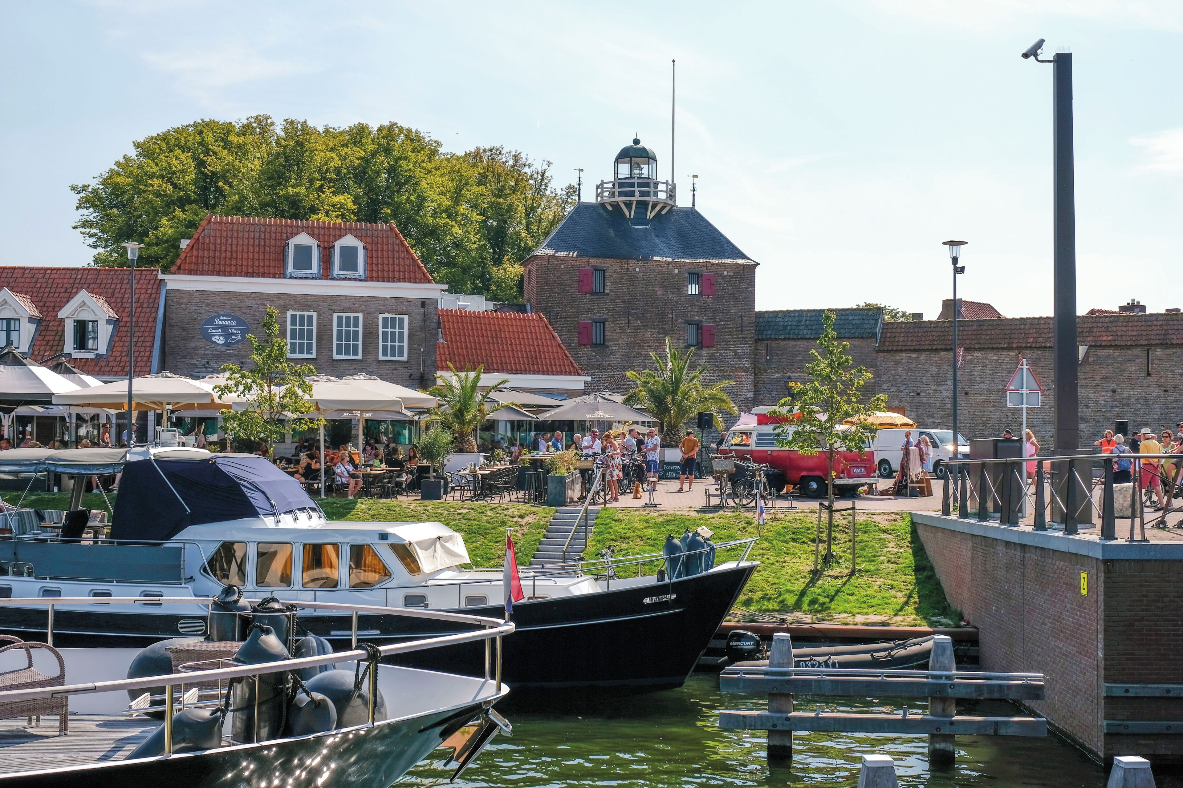 A waterfront area with boats docked, a historic building, and a public space with people.
