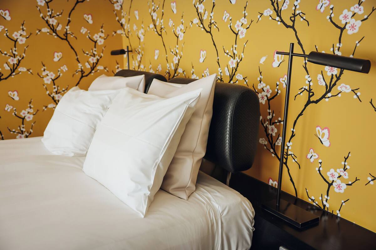 Ein Bett mit weißer Bettwäsche und einem schwarzen Kopfteil, ein Nachttisch mit einer Lampe und eine Wand mit einem Blumenmuster.