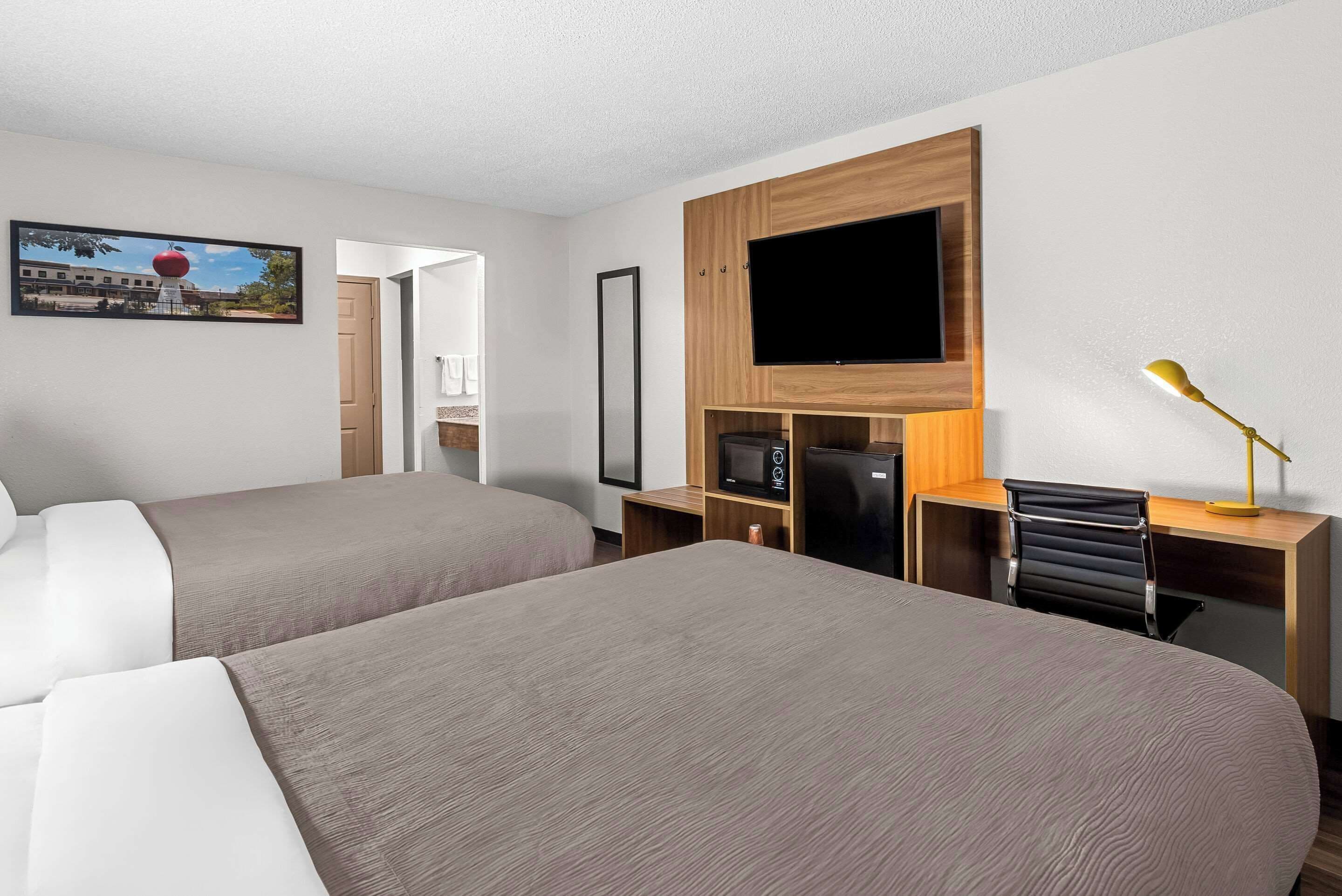 Una habitación de hotel con dos camas, una televisión, un escritorio con computadora y una lámpara.