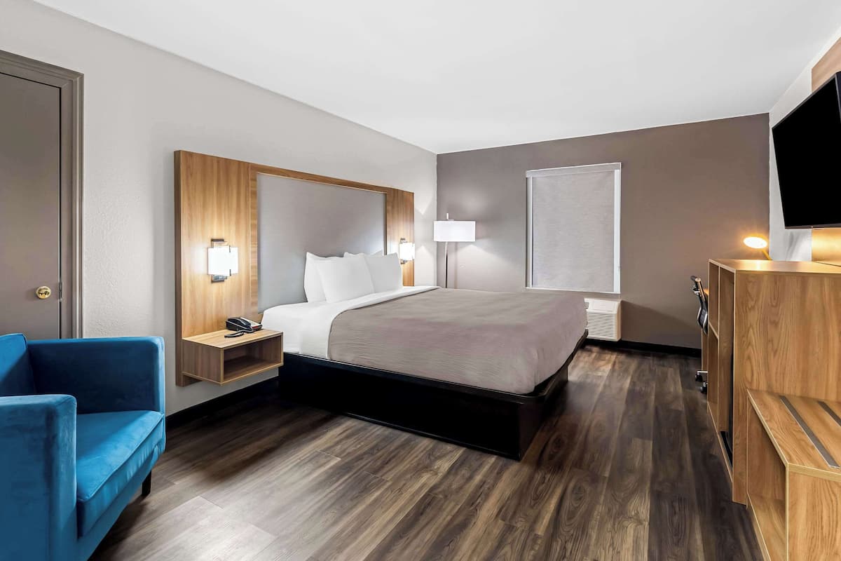 A hotel room with a bed, bedside tables, a desk, a chair, a TV, and a wardrobe.